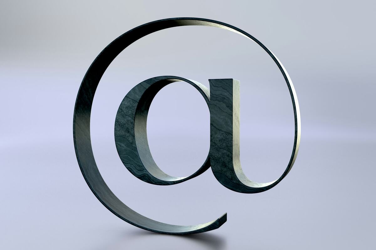 A 3D-rendered metallic @ symbol standing on a plain background