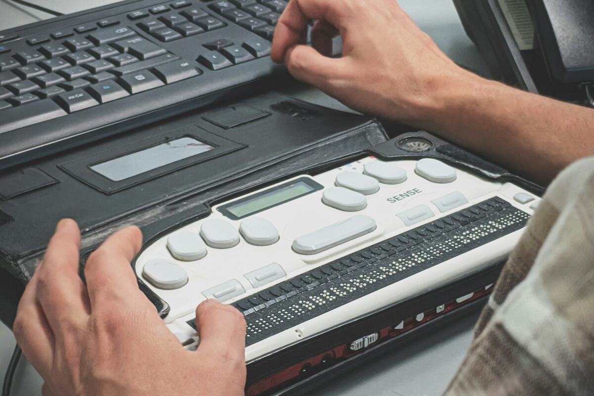 Hands using a braille display note-taker next to a computer keyboard